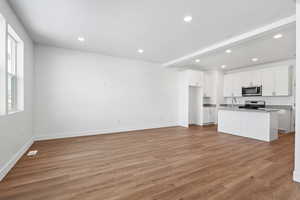 Kitchen with appliances with stainless steel finishes, white cabinetry, sink, a center island with sink, and light wood-type flooring