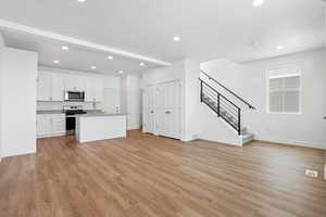 Kitchen with beamed ceiling, white cabinets, stainless steel appliances, a center island with sink, and light hardwood / wood-style flooring