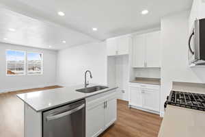 Kitchen featuring appliances with stainless steel finishes, sink, white cabinets, a kitchen island with sink, and light hardwood / wood-style flooring