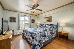 Bedroom with hardwood / wood-style flooring, baseboard heating, ceiling fan, and crown molding