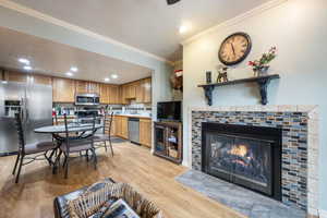 Kitchen with appliances with stainless steel finishes, ornamental molding, tasteful backsplash, a fireplace, and light wood-type flooring