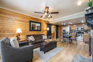 Living room with wood walls, crown molding, ceiling fan, and light hardwood / wood-style flooring