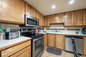 Kitchen featuring sink, light wood-type flooring, appliances with stainless steel finishes, and tasteful backsplash