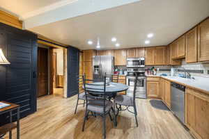 Kitchen with stainless steel appliances, sink, light wood-type flooring, and decorative backsplash