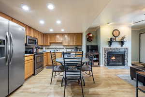 Kitchen featuring a stone fireplace, crown molding, backsplash, light wood-type flooring, and appliances with stainless steel finishes