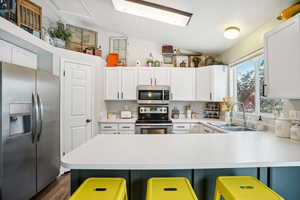 Kitchen with appliances with stainless steel finishes, a breakfast bar, vaulted ceiling, sink, and white cabinetry