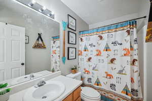 Bathroom featuring a shower with curtain, vanity, toilet, and a textured ceiling