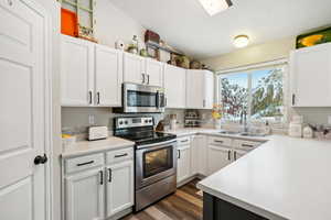 Kitchen featuring dark hardwood / wood-style flooring, sink, white cabinets, and appliances with stainless steel finishes