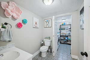 Bathroom with toilet, washing machine and dryer, vanity, and a textured ceiling