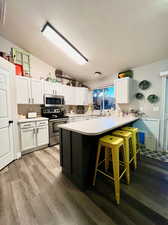 Kitchen with kitchen peninsula, appliances with stainless steel finishes, a breakfast bar area, lofted ceiling, and white cabinets