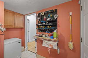 Laundry area with light tile patterned flooring and a textured ceiling