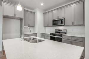 Kitchen with dark wood-type flooring, sink, gray cabinets, pendant lighting, and appliances with stainless steel finishes