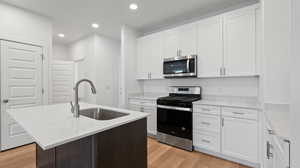 Kitchen with white cabinetry, appliances with stainless steel finishes, a kitchen island with sink, and sink