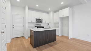 Kitchen with sink, appliances with stainless steel finishes, white cabinetry, light hardwood / wood-style floors, and an island with sink