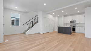 Kitchen featuring light hardwood / wood-style flooring, an island with sink, beamed ceiling, stainless steel appliances, and white cabinets