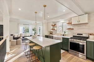 Kitchen with stainless steel range with gas cooktop, green cabinetry, light hardwood / wood-style flooring, white cabinets, and decorative backsplash