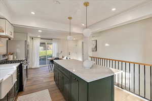 Kitchen featuring hardwood / wood-style flooring, stainless steel range with gas stovetop, white cabinetry, a kitchen island, and pendant lighting