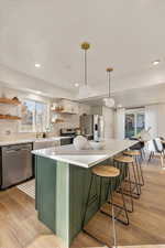 Kitchen with stainless steel appliances, backsplash, hanging light fixtures, white cabinets, and light hardwood / wood-style flooring