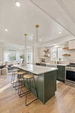 Kitchen featuring white cabinetry, stainless steel stove, green cabinetry, hanging light fixtures, and light hardwood / wood-style floors