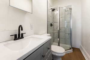 Bathroom with hardwood / wood-style floors, a shower with shower door, vanity, and toilet