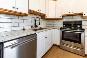 Kitchen with stainless steel appliances, light hardwood / wood-style floors, sink, white cabinets, and decorative backsplash