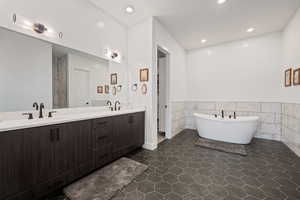 Bathroom with tile walls, vanity, tile patterned floors, and a tub