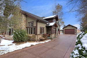 View of snow covered exterior featuring a garage and an outdoor structure