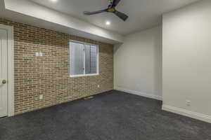 Spare room featuring ceiling fan, brick wall, and dark colored carpet