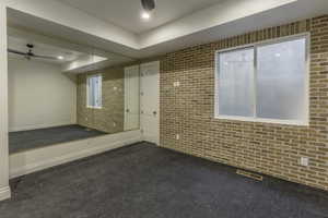 Unfurnished room with a tray ceiling, dark carpet, and brick wall