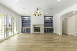 Unfurnished living room with a high end fireplace, built in shelves, light hardwood / wood-style floors, and french doors