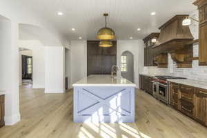 Kitchen featuring backsplash, range with two ovens, sink, decorative light fixtures, and light hardwood / wood-style floors