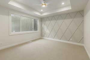 Empty room featuring carpet, a tray ceiling, and ceiling fan