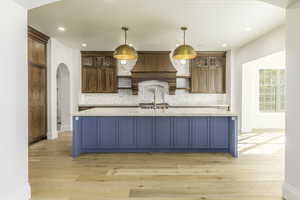 Kitchen with premium range hood, decorative backsplash, light hardwood / wood-style floors, and decorative light fixtures