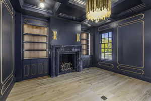 Unfurnished living room featuring coffered ceiling, built in shelves, crown molding, hardwood / wood-style flooring, and beamed ceiling