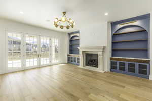 Unfurnished living room featuring french doors, an inviting chandelier, hardwood / wood-style flooring, a premium fireplace, and built in features