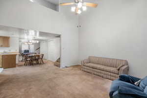 Carpeted living room featuring sink, a towering ceiling, and ceiling fan with notable chandelier