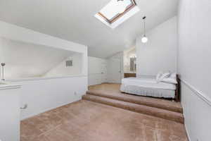 Bedroom featuring vaulted ceiling with skylight, ensuite bath, and carpet floors