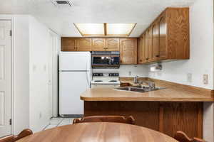 Kitchen with kitchen peninsula, a textured ceiling, sink, light tile patterned floors, and white appliances