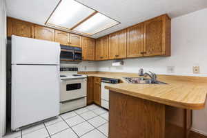 Kitchen featuring light tile patterned floors, white appliances, sink, and kitchen peninsula