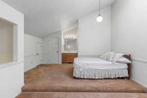 Bedroom featuring carpet, a textured ceiling, vaulted ceiling, and connected bathroom