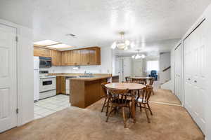 Kitchen with kitchen peninsula, a textured ceiling, light carpet, white appliances, and decorative light fixtures