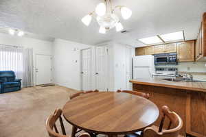 Carpeted dining room with sink, a textured ceiling, and a notable chandelier