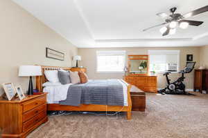 Bedroom with carpet floors, ceiling fan, and a raised ceiling