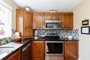 Kitchen with dark stone counters, decorative backsplash, and stainless steel appliances