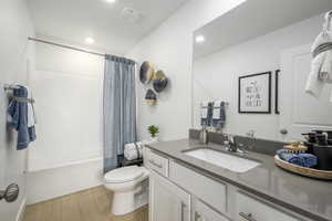 Full bathroom featuring hardwood / wood-style floors, vanity, shower / bathtub combination with curtain, and toilet