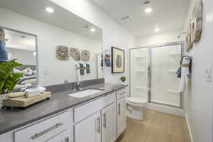 Bathroom featuring toilet, vanity, hardwood / wood-style floors, and a shower with door