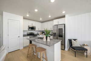 Kitchen featuring light wood-type flooring, appliances with stainless steel finishes, an island with sink, white cabinets, and a breakfast bar area