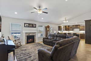 Living room featuring a stone fireplace, ceiling fan with notable chandelier, light hardwood / wood-style flooring, and lofted ceiling