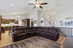 Living room featuring light hardwood / wood-style floors, ceiling fan with notable chandelier, and high vaulted ceiling