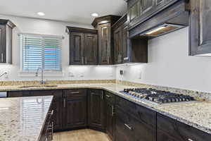 Kitchen with light stone counters, stainless steel gas cooktop, sink, light wood-type flooring, and premium range hood